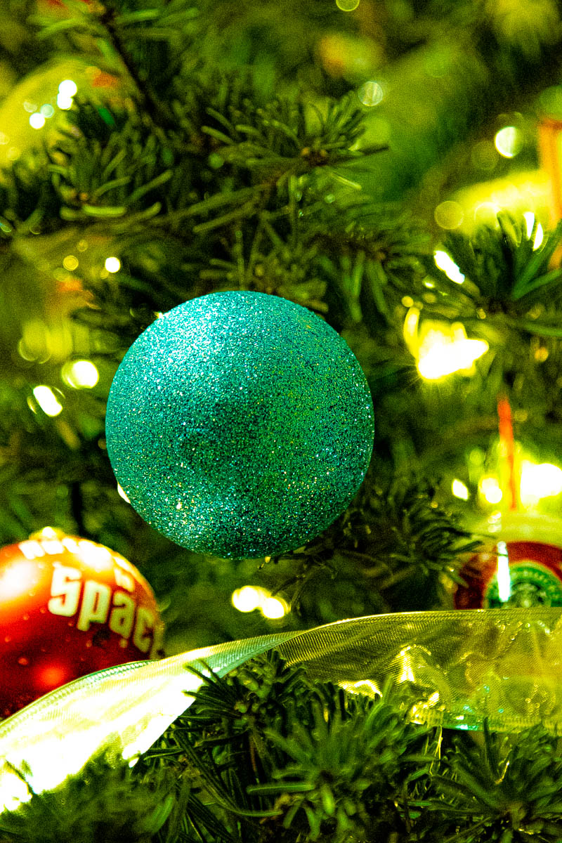 Christmas ornament close-up — teal glitter ball on a lit tree